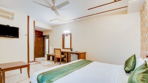 A hotel room with a bed, a desk, a chair, a television, a ceiling fan, and a wardrobe. - Itsy Hotels Auzone & Spa (Chandigarh)