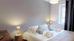 Un dormitorio con cama, lámparas de noche, una mesita de noche de madera y una ventana con cortinas.