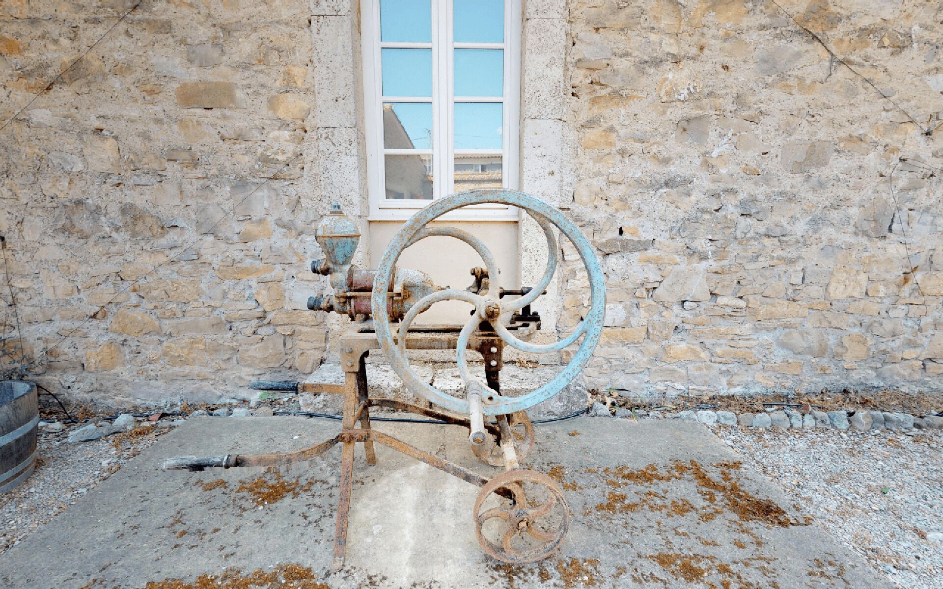 An old water pump with a hose, a window, and stone walls.