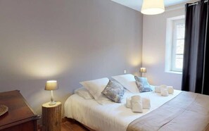 Un dormitorio con cama, lámparas de noche, una mesita de noche de madera y una ventana con cortinas.