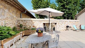 Un patio con una mesa redonda de metal y sillas, una sombrilla blanca y un muro de piedra.