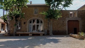 Un edificio de piedra con un amplio ventanal arqueado, una banca en el exterior y un patio de grava.