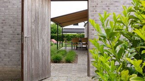 An open wooden door leading to a covered outdoor seating area with chairs and a table, set against a brick wall. - Polderwoning Cleylantshof max. 8 p midden in de polders van het Meetjesland. (Watervliet)
