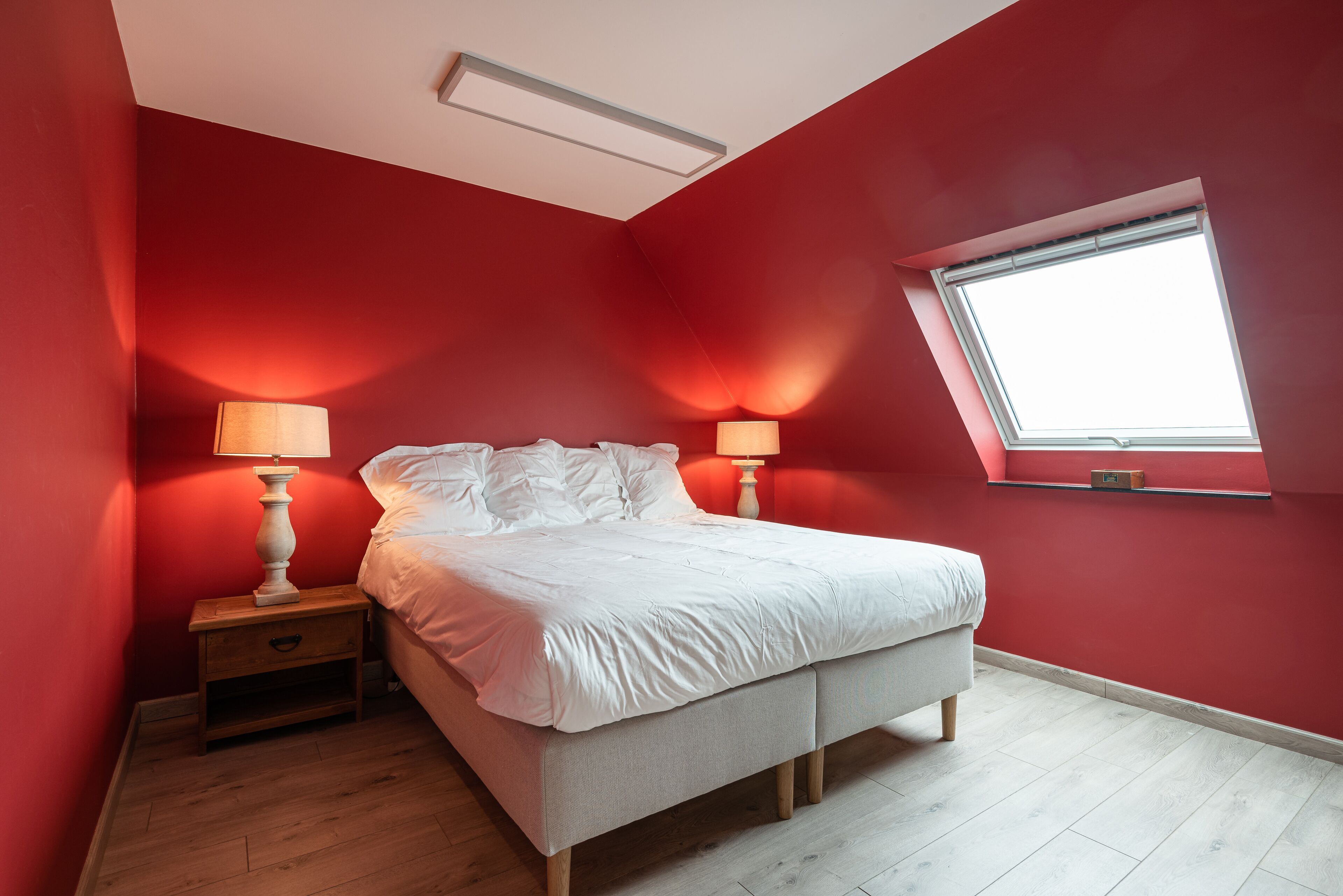 A bedroom with a bed, two bedside tables with lamps, a window, and a sloped ceiling.