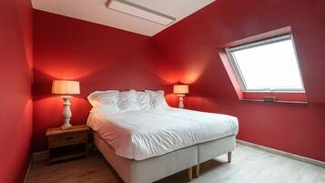 A bedroom with a bed, two bedside tables with lamps, a window, and a sloped ceiling.
