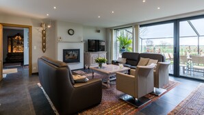 A spacious living room with a large window, a fireplace, and a television. - Polderwoning Cleylantshof max. 8 p midden in de polders van het Meetjesland. (Watervliet)