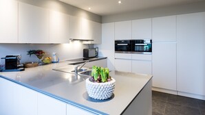 A modern kitchen with white cabinets, stainless steel appliances, and a central island with a decorative plant. - Polderwoning Cleylantshof max. 8 p midden in de polders van het Meetjesland. (Watervliet)