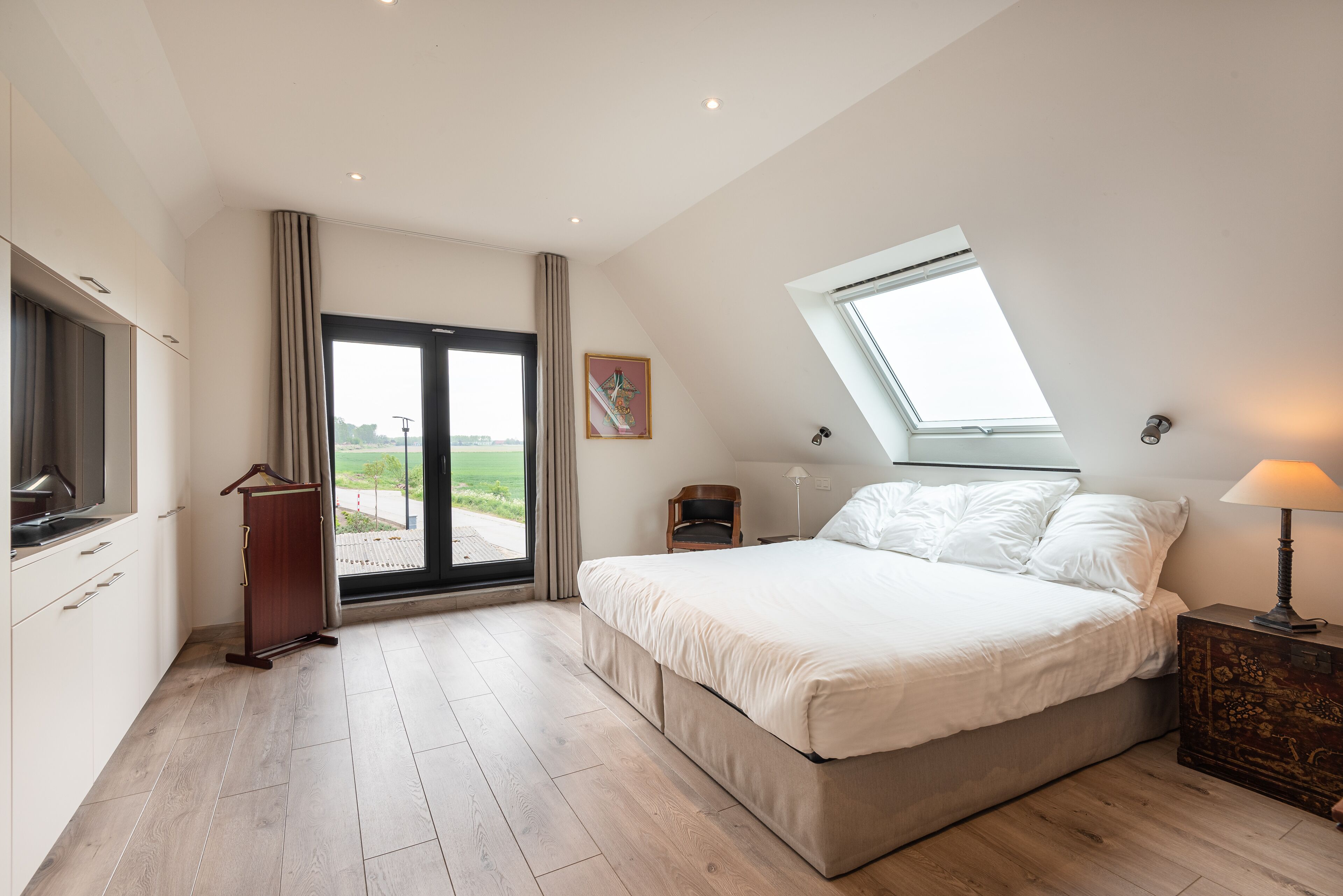 A bedroom with a large bed, a skylight, a desk, and a view of the outdoors.