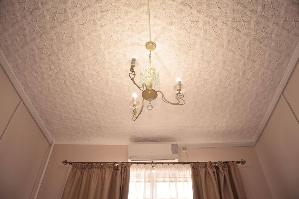 A room with a patterned ceiling, a chandelier, an air conditioning unit, and curtains.