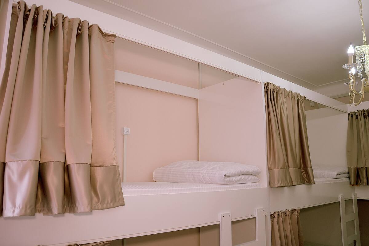 A bunk bed room with beige curtains, a chandelier, and a white wall.