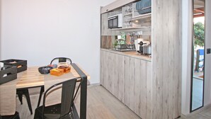 A modern kitchen with wooden cabinets, a microwave, and a dining area with a wooden table and chairs. - Camara Studio Mykonos (Mykonos)