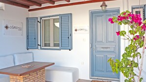 A room with a wooden table, a bench, and a blue door with a bell. - Camara Studio Mykonos (Mykonos)