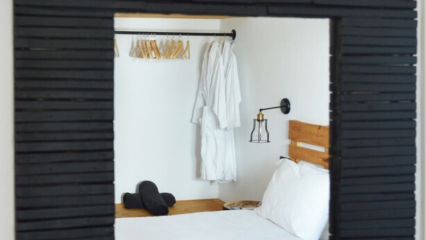A bedroom with a bed, a hanging robe rack, and a wall-mounted lamp. - Camara Studio Mykonos (Mykonos)