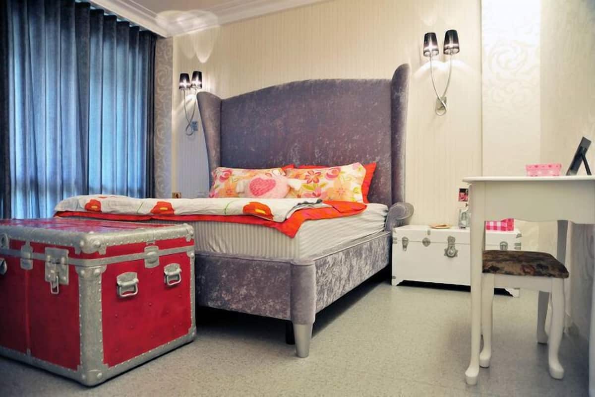 A bedroom with a bed, a red suitcase, a white dresser, and a chair.