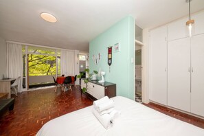A hotel room with a large bed, a desk, a chair, and a view of trees through a window.