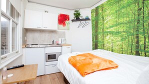 A compact room with a bed, a small kitchenette, and a large window with a forest view. - Cosy Studio in the Heart of Trendy Kemptown (Brighton)