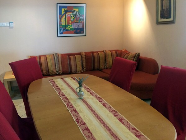 Un comedor con una mesa de madera, sillas tapizadas en rojo y un mantel a rayas. Un cuadro colorido está en la pared sobre la mesa.