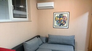 A corner room with a grey sofa, a red pillow, and a framed artwork on the wall. - Apartments Bogdanovic (Maribor)