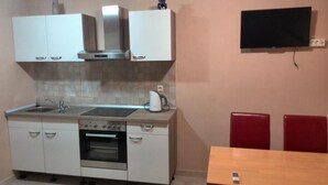 A compact kitchen with a stove, oven, and microwave, a sink, and a flat-screen TV mounted on the wall. - Apartments Bogdanovic (Maribor)