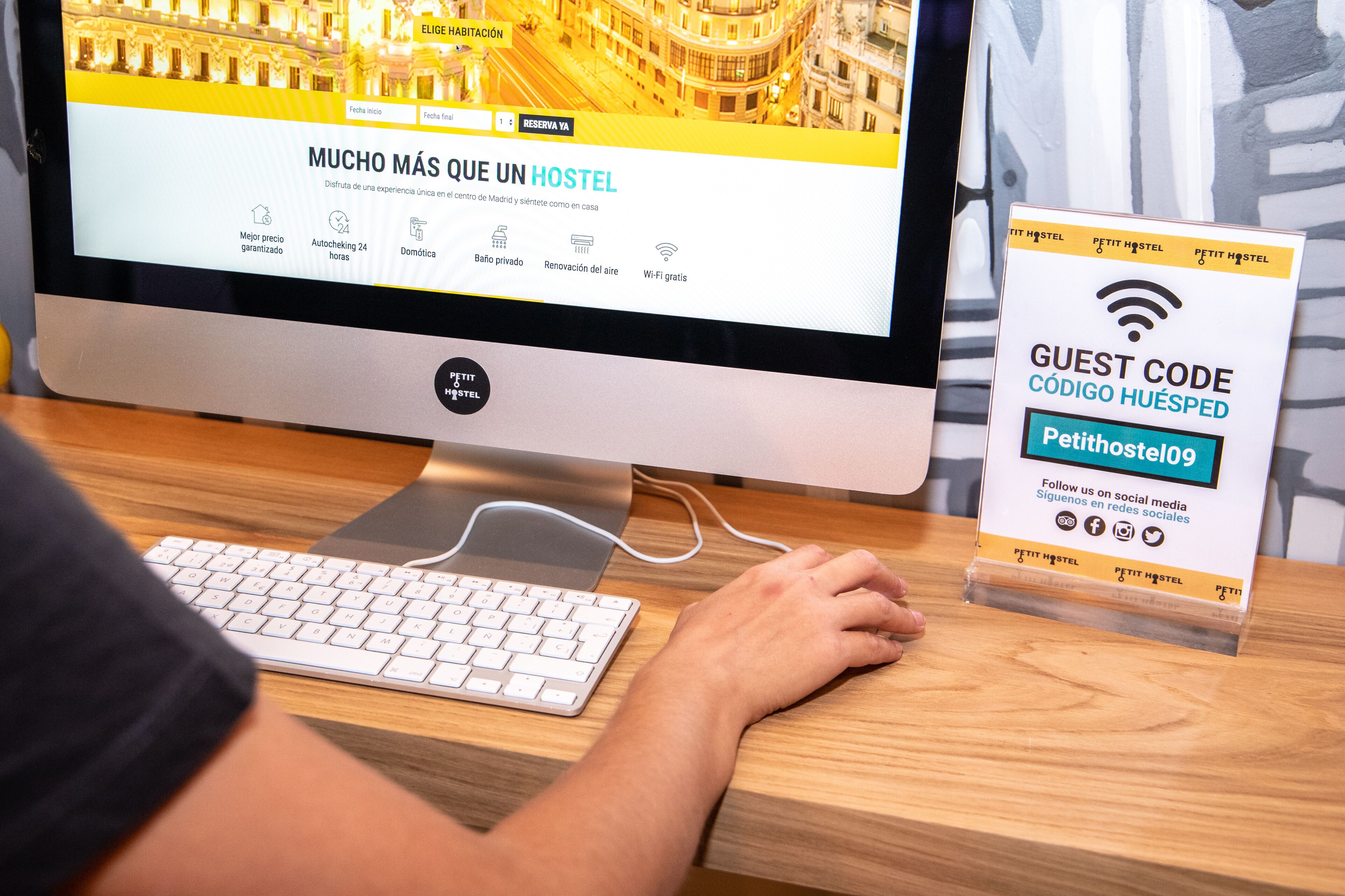 Un monitor de computadora que muestra un sitio web de hotel con un cartel de código de invitado sobre un escritorio.