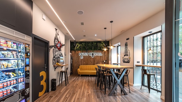 Interior moderno de un albergue con una máquina expendedora, un sofá y una pared de madera con plantas.