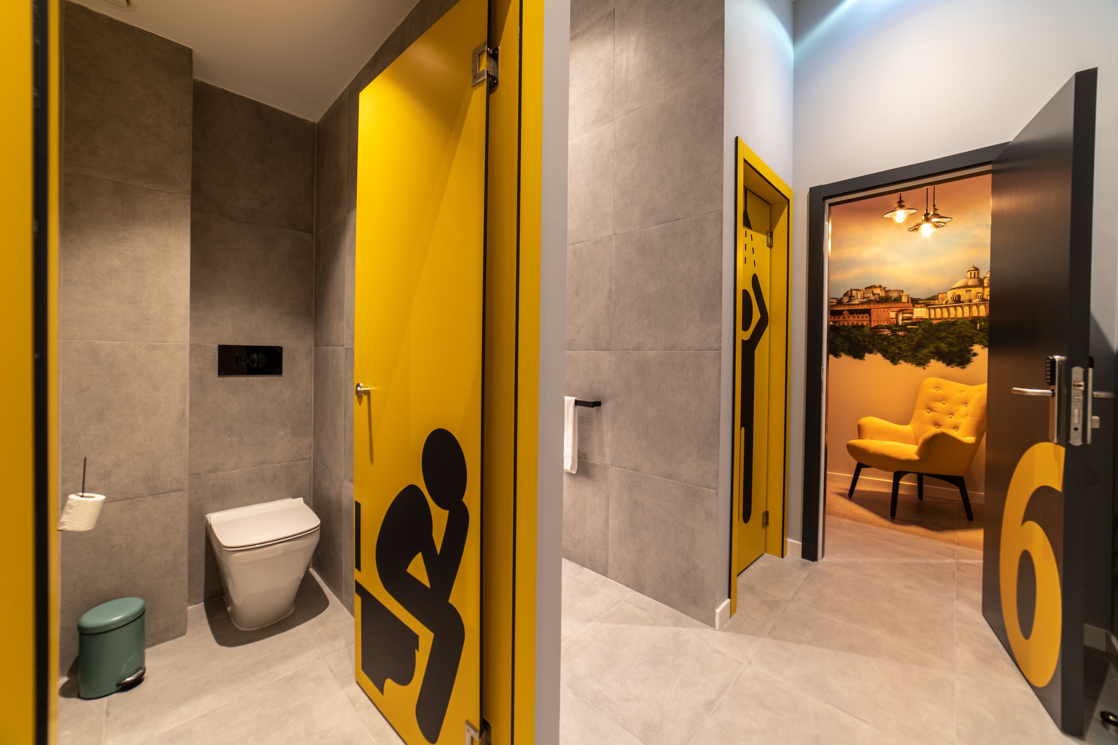 Une salle de bain moderne avec un mur d’accent jaune, des toilettes, une poubelle et un lavabo.