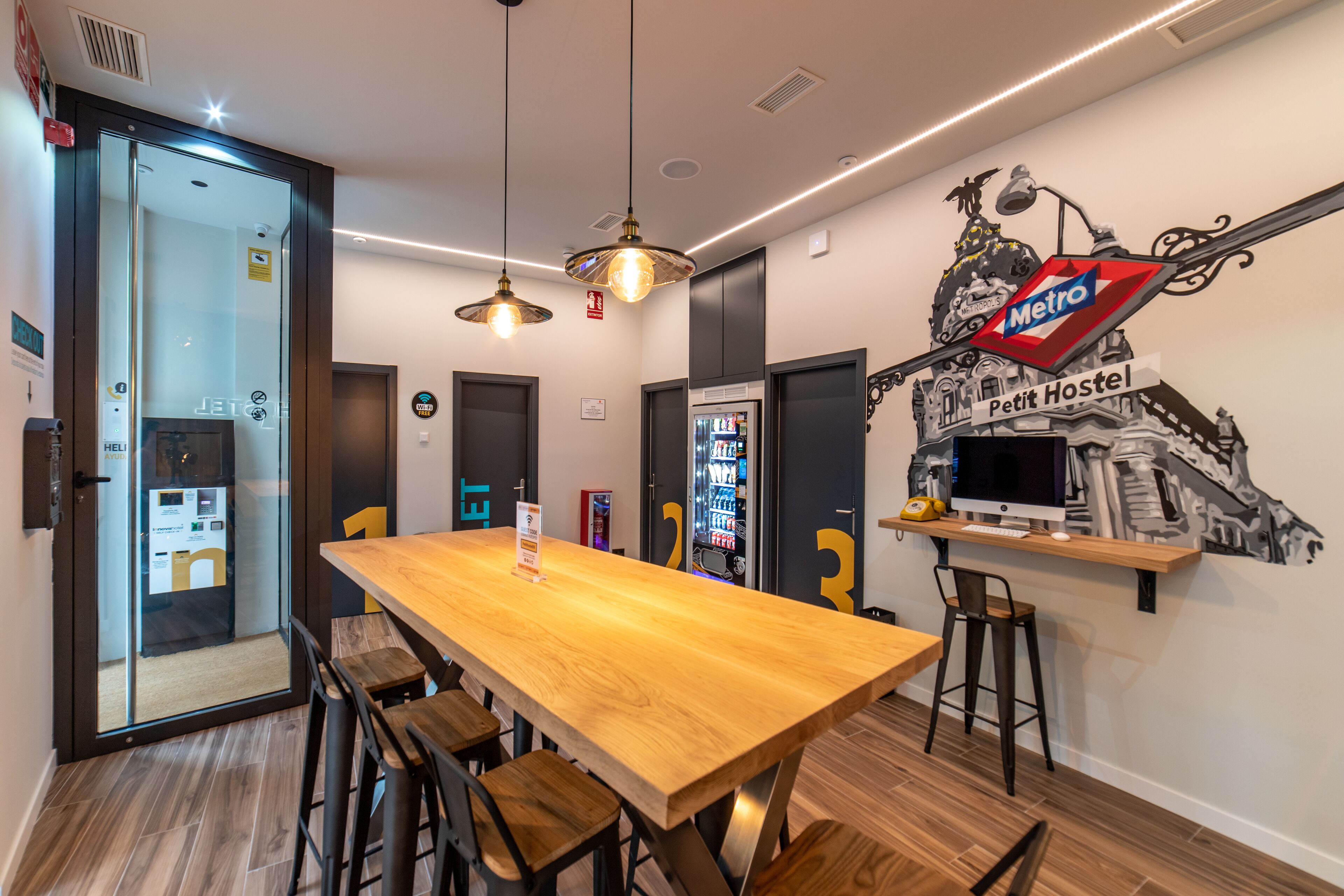 A modern room with a wooden table, bar stools, a computer, and a wall mural.