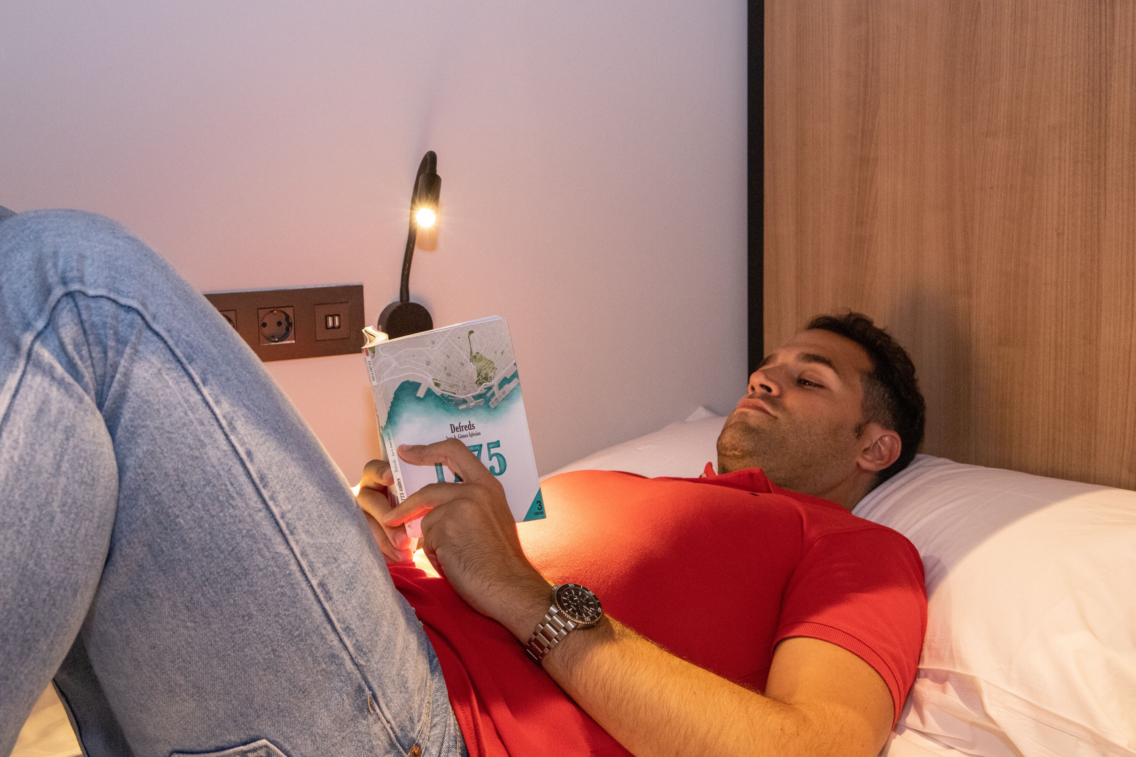 Una persona acostada en la cama leyendo un libro.