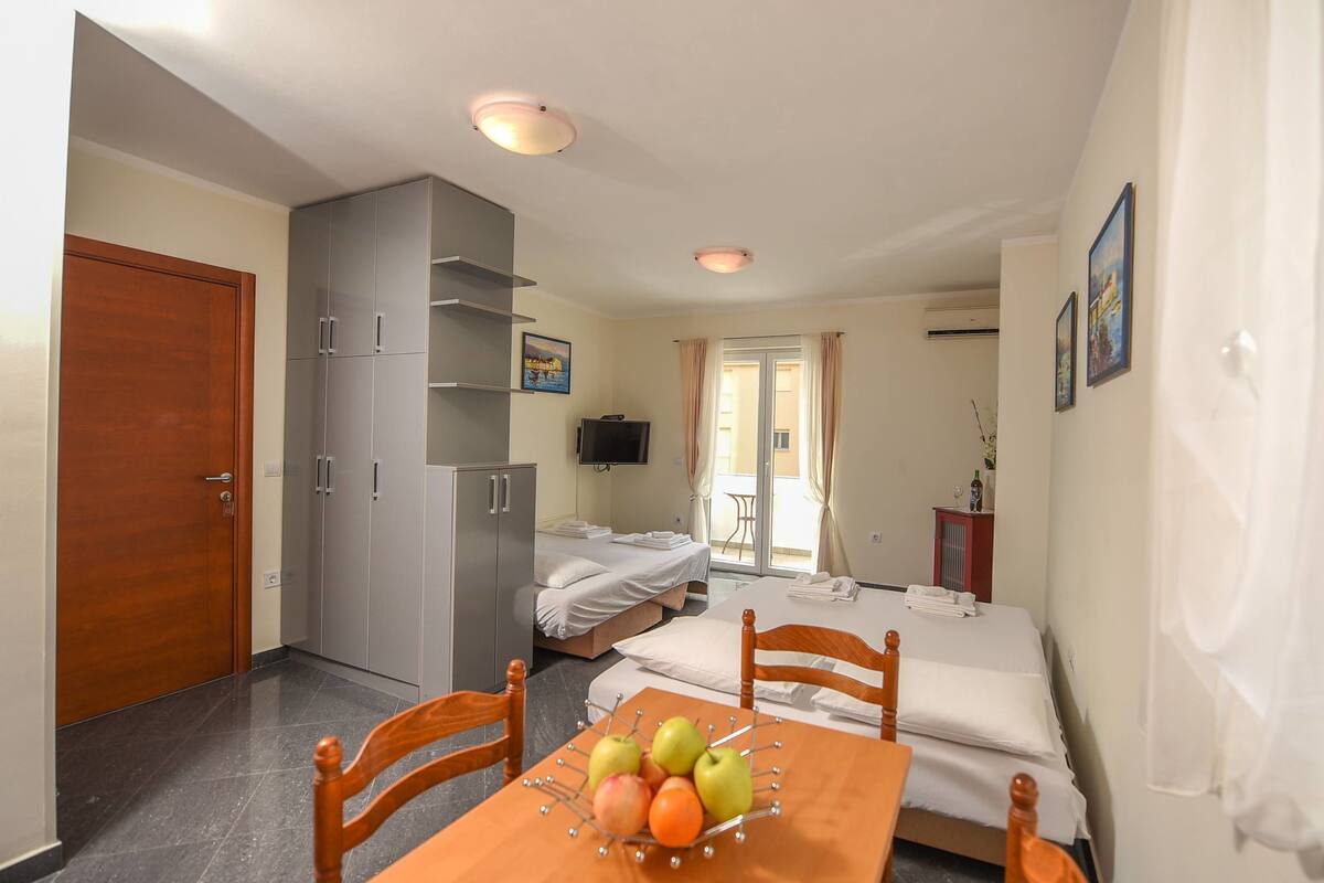 Habitación de hotel con una mesa de madera, sillas, una cama, televisor y balcón con cortinas.