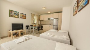 Una habitación de hotel con dos camas, televisión, una pequeña cocina y comedor.