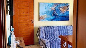 A small living room with a wooden door, a sofa, a table with a lamp, and a painting on the wall.