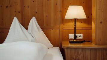 A wooden-paneled room with a bed, white pillows, and a table lamp.