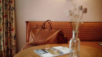 Une pièce avec une table en bois, un sac en cuir marron, un vase contenant des fleurs séchées et un canapé à motifs.