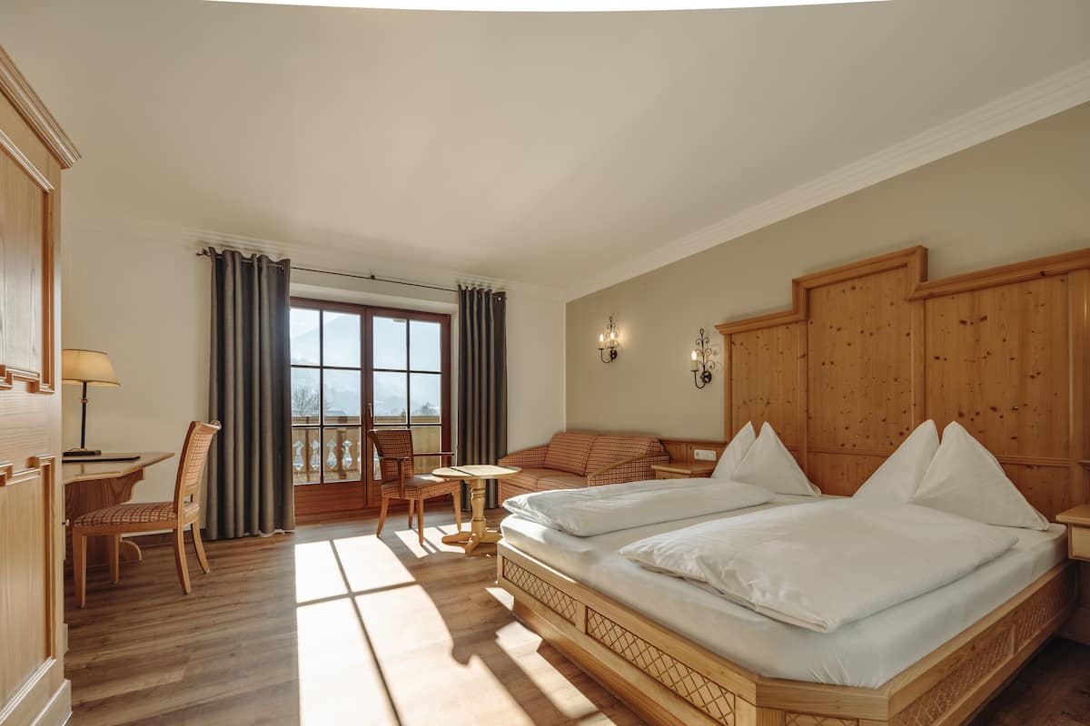 Habitación de hotel con una cama grande, un escritorio con silla, una mesita y un balcón con vistas.
