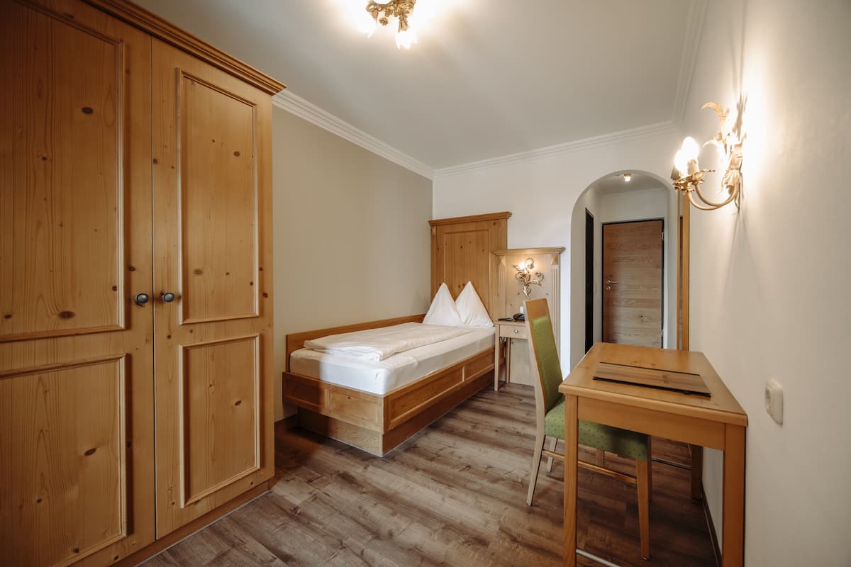Un dormitorio con cama de madera, escritorio y silla. Se observa un armario y un espejo en la pared.