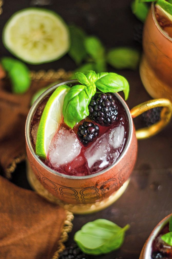 Ein Glas mit Eiswürfeln, Brombeeren und einer Limettenscheibe, garniert mit einem Basilikumblatt.
