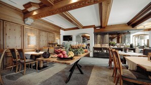 Un comedor amplio con mesas y sillas de madera, una presentación central de frutas y una cocina al fondo.