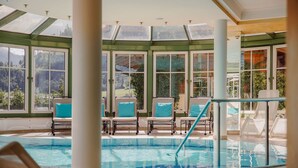 Una piscina interior con paredes de vidrio transparente, múltiples sillones de descanso y vistas a un paisaje montañoso.