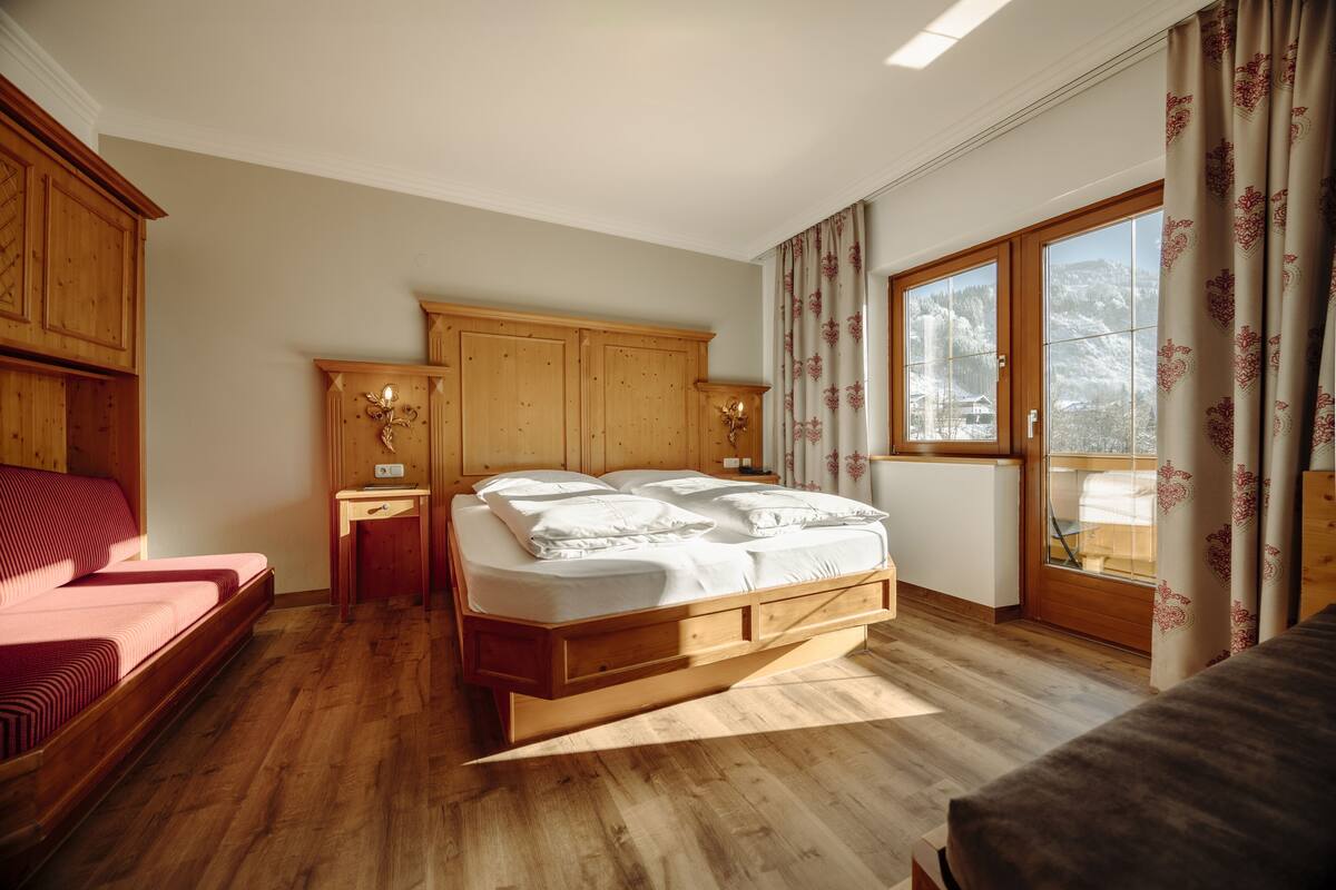 Un dormitorio con una cama y un armario de madera, una mesita de noche y una ventana con cortinas.
