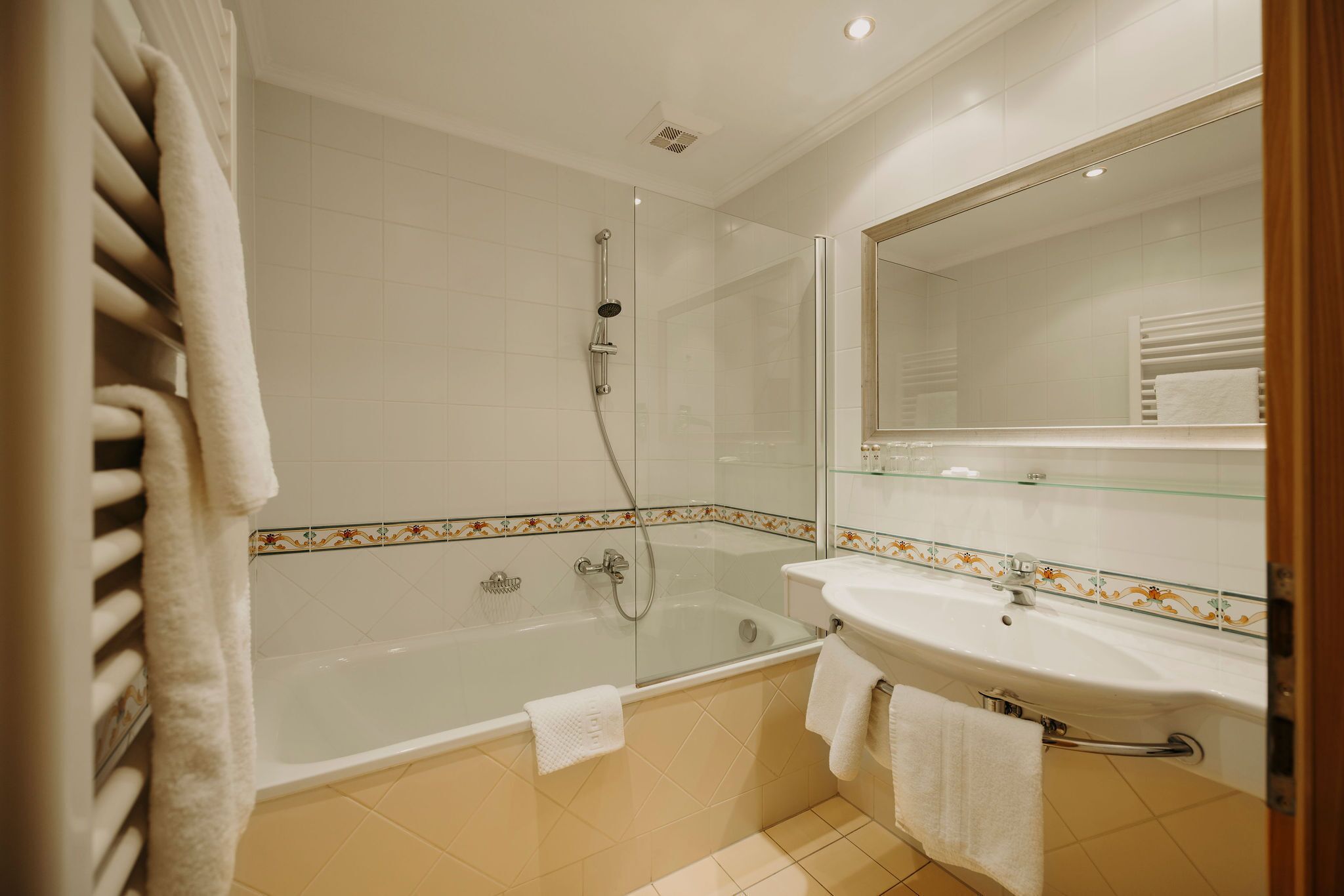 A modern bathroom with a glass-enclosed shower, a white bathtub, and a sink with a glass shelf above.