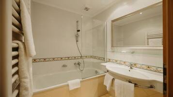 A modern bathroom with a glass-enclosed shower, a white bathtub, and a sink with a glass shelf above.