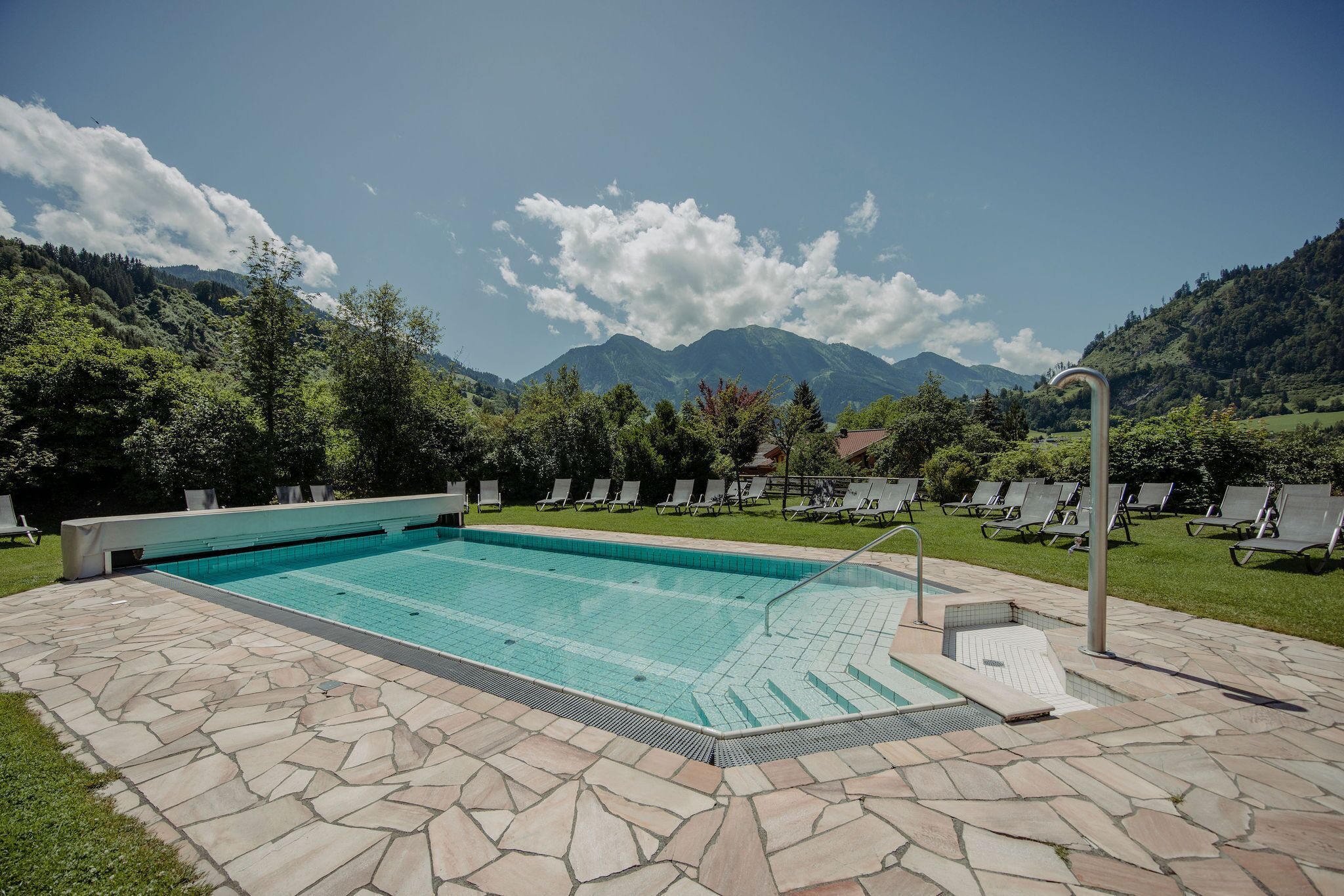 Piscina con baldosas de piedra, rodeada de sillas de descanso y vistas a montañas.