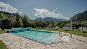 Piscina con baldosas de piedra, rodeada de sillas de descanso y vistas a montañas.