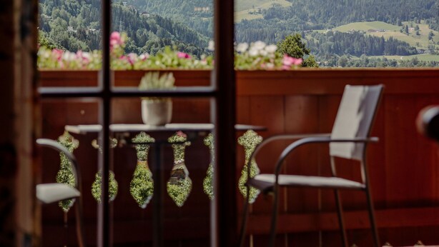 Un balcón con vistas a montañas, una silla y una mesa con un florero y flores.