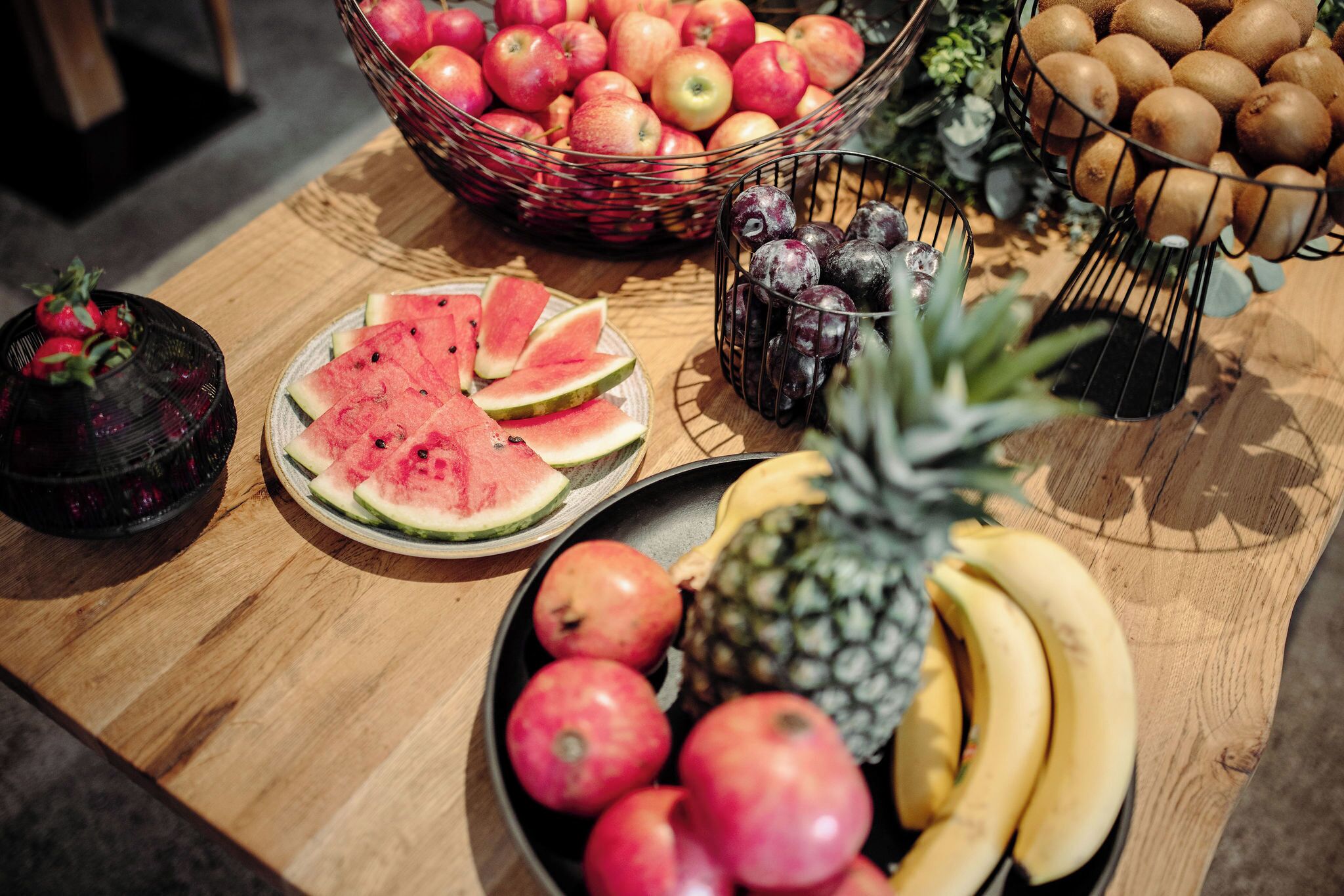 Ein Holztisch mit verschiedenen Früchten, darunter Äpfel, Bananen und Wassermelonenscheiben.
