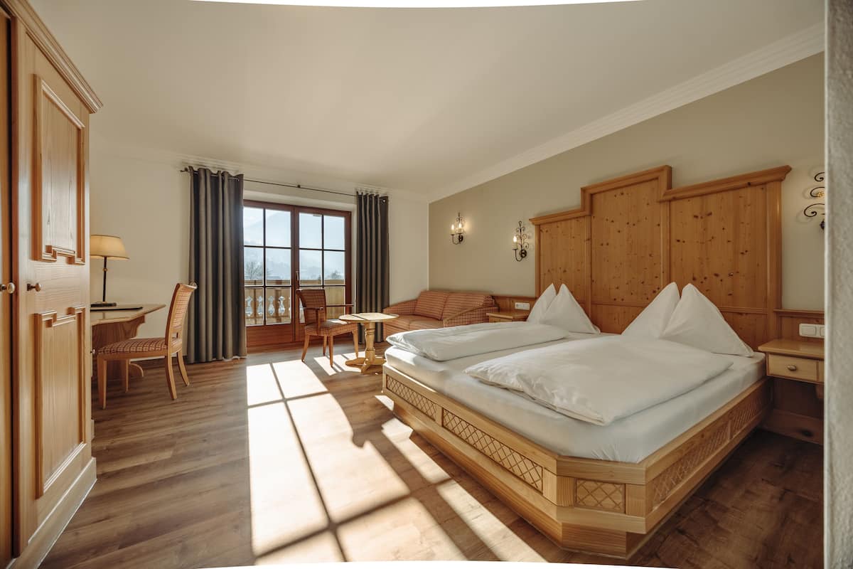 Habitación de hotel con una cama grande, un armario de madera, un escritorio con silla y vistas al exterior.