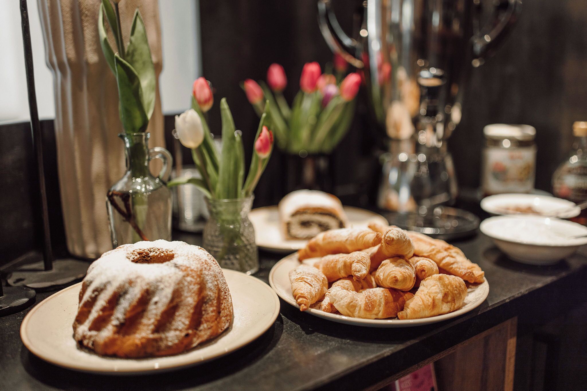 A buffet table with a bundt cake, croissants, and a plate of sushi.