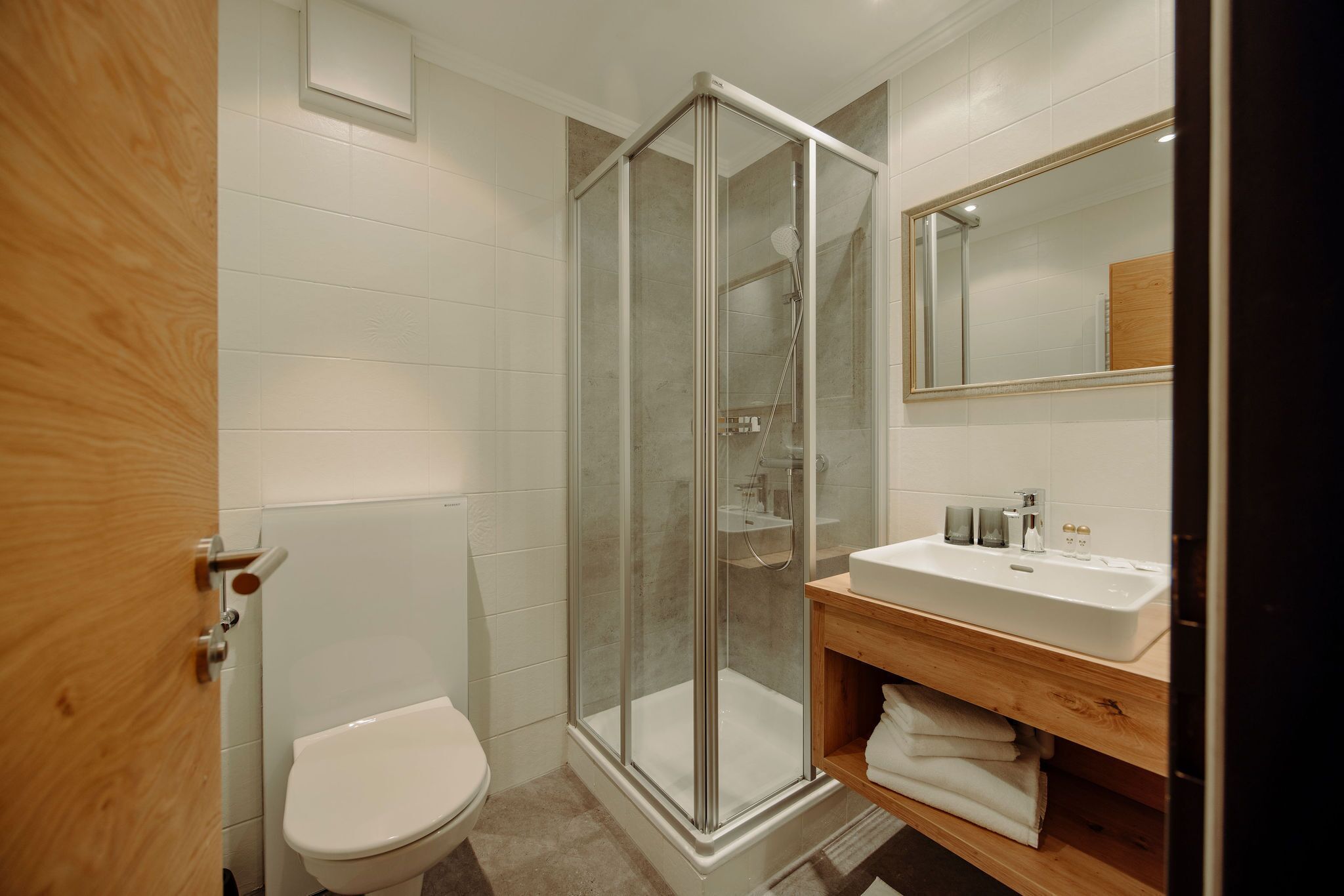 Un baño moderno con ducha de vidrio, inodoro blanco y tocador de madera con lavamanos.