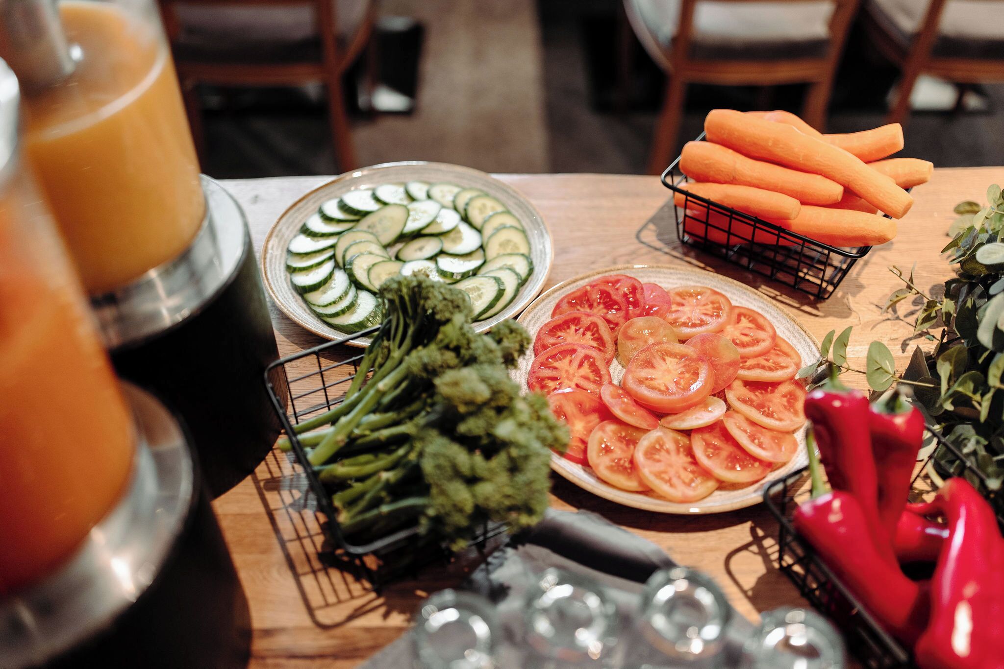 A table with sliced vegetables, a basket of carrots, and a glass pitcher.