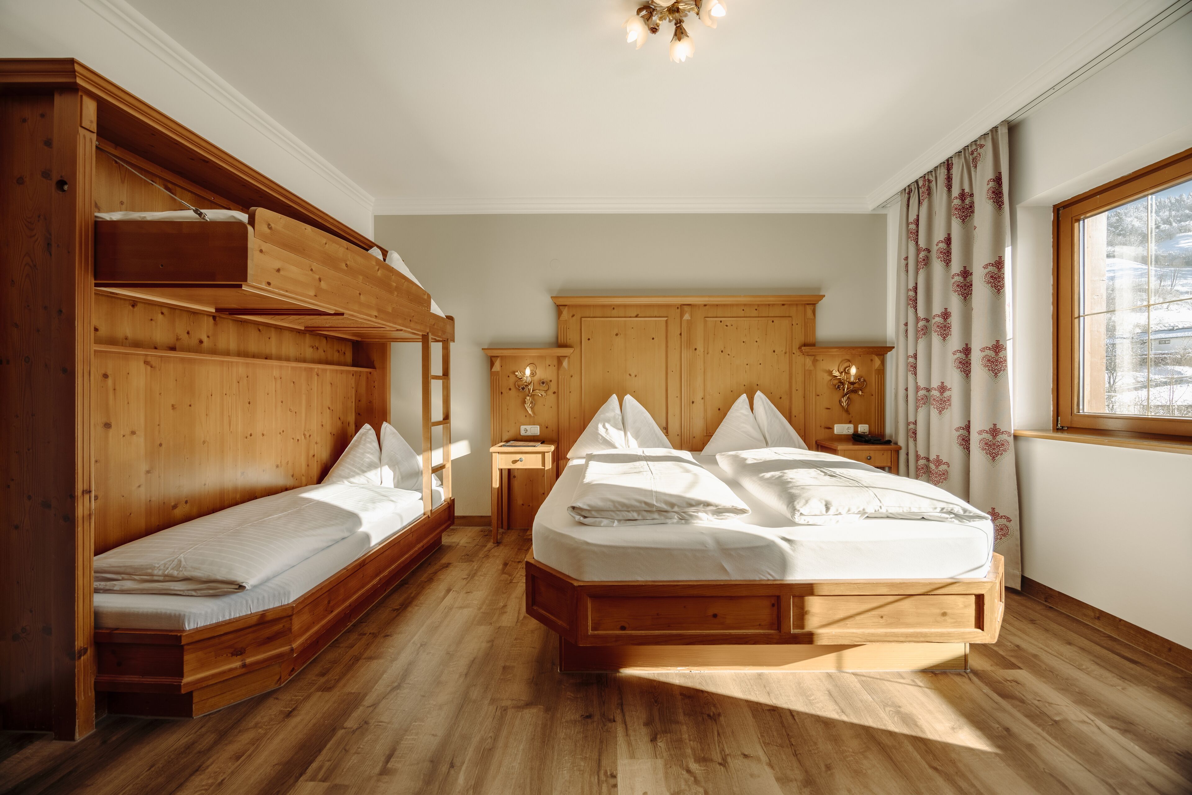 Ein Schlafzimmer mit Etagenbett, einem Einzelbett, Holzboden, einem Fenster mit Vorhängen und einem Holz-Kopfteil.